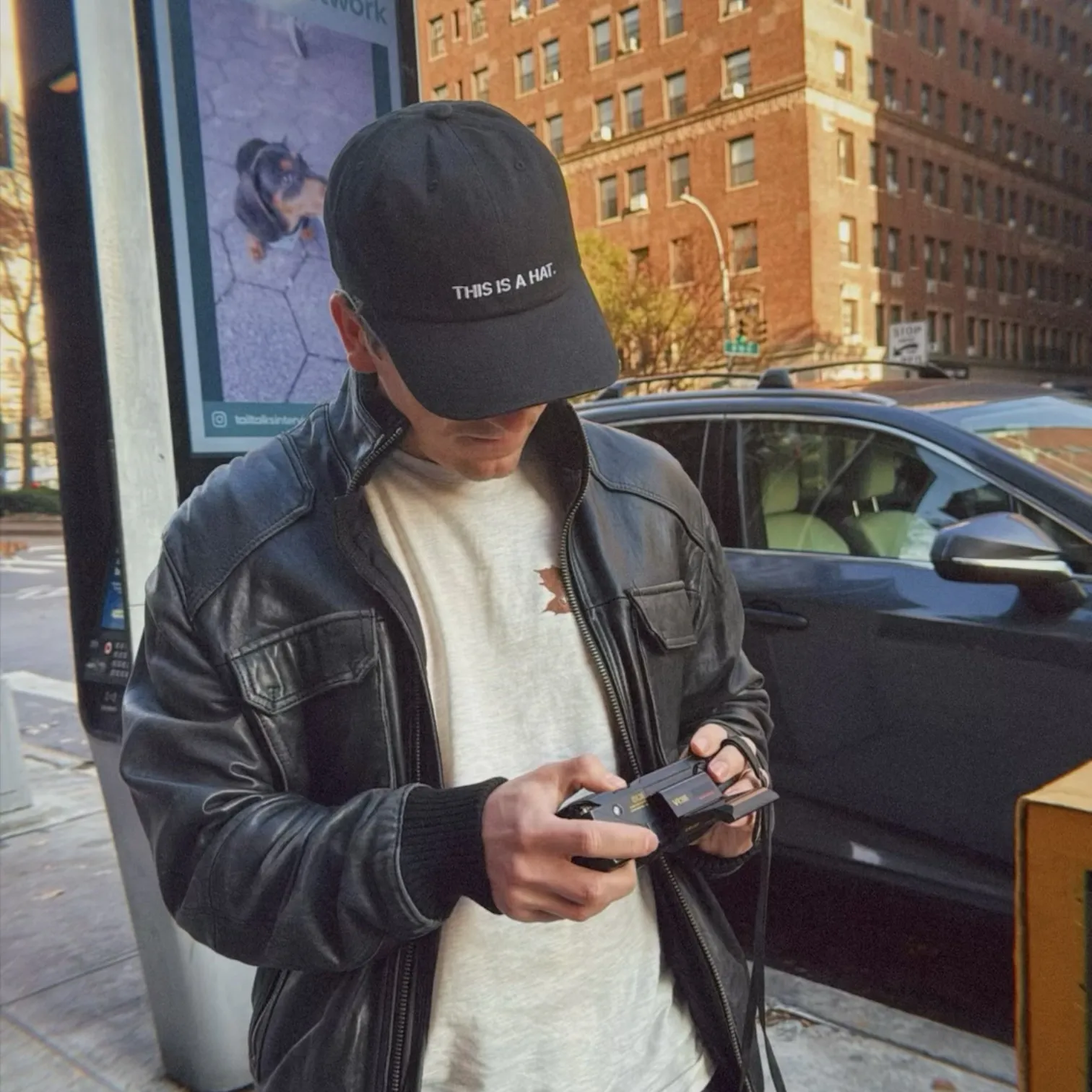 Person wearing black hat that says THIS IS A HAT outdoors in NYC.